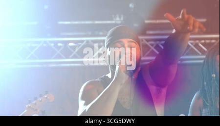 Ein packendes Mikrofon, der Sänger streckt sich auf die Bühne unter einem Metalltrakt mit Lichtern und Gitarrenhals Stockfoto