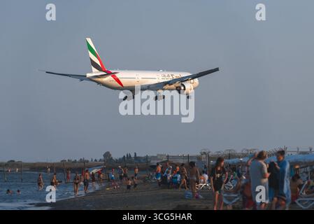 Larnaca, Zypern - 26. Juli 2025: Touristen genießen den Strand in Mackenzie, Larnaca, beobachten Boeing 777 der Emirates Airline Flugzeuge, die in Larnaca landen Stockfoto
