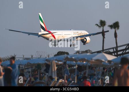 Larnaca, Zypern - 26. Juli 2025: Touristen genießen den Strand in Mackenzie, Larnaca, beobachten Boeing 777 der Emirates Airline Flugzeuge, die in Larnaca landen Stockfoto