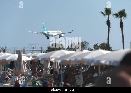 Larnaca, Zypern - 26. Juli 2025: Passagier-Airbus A220-300 der Cyprus Airways Airways Airplane landet über Mackenzie Strand voller Touristen, die den Sommer genießen Stockfoto