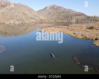 Skadar Lake (TGD), Montenegro – 2020.11.08: Dritter afrikanischer Kulturreisender mit einheimischen Fischern, die die Feuchtgebiete der Vranjina in einem Holzboot überqueren. Stockfoto