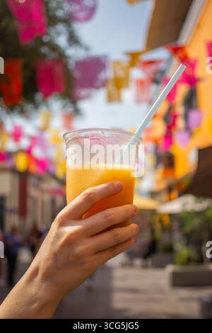 Kommerzielles Foto einer Hand mit einem Tejuino, traditionelles mexikanisches fermentiertes Maisgetränk mit Eis, erfrischendes Sommergetränk an einem sonnigen Tag mit Farbtönen Stockfoto