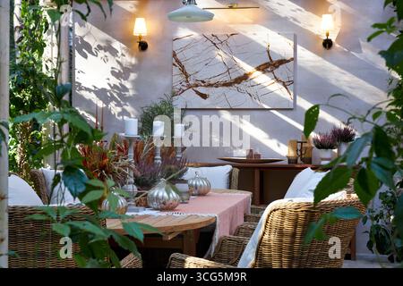 Stilvoller Essbereich im Freien mit Korbstühlen, Holztisch, Kerzen und Herbstdekor. Umgeben von Grün, kombiniert diese gemütliche Terrasse rustikales Eleg Stockfoto