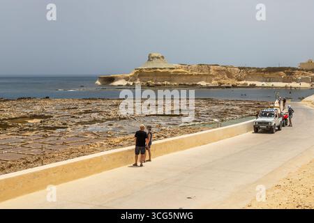 Gozo, Malta – 23. Juni 2021: Touristen stehen an den Salinen, während ein Auto die Küstenstraße entlang fährt. Stockfoto