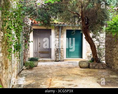 Zwei verschiedene Türen mit Baum in ruhigem Steinhof. Architektur, urbane Ruhe und kulturelle Tradition in mediterraner Wohnstraße. Stockfoto