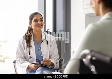 Glücklicher junger indischer Rehabilitationsarzt im weißen Fell, der eine Beratung gibt Stockfoto