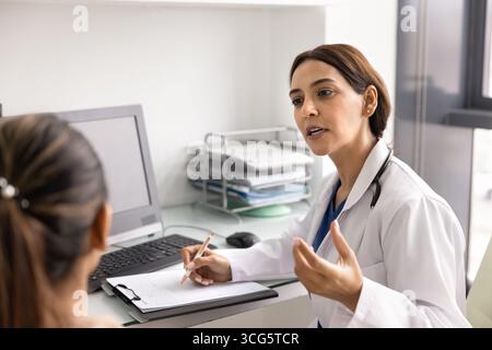Ernsthafter Arzt aus dem Nahen Osten im Gespräch mit weiblicher Patientin am Arbeitsplatz Stockfoto