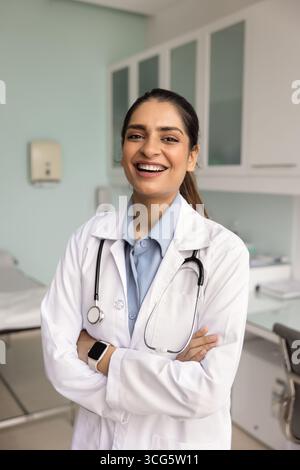 Fröhliche, selbstbewusste junge indische Ärztin, die mit gefalteten Händen steht Stockfoto