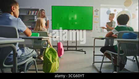 Grundschuljunge mit Tablet-Computer, der Wissen vor Klassenkameraden und Lehrer mithilfe des digitalen Bildschirms mit Chromakey Mockup präsentiert. Platzhalter für den grünen Bildschirm für interaktive visuelle Effekte. Stockfoto