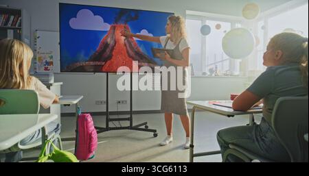 Grundschüler Studieren Grundlegende Informationen Über Den Vulkanausbruchprozess. Lehrerin mit Tablet-Computer erklärt Smart Kids Geologie und Wissenschaft mithilfe des digitalen Bildschirms. Dolly Shot Stockfoto