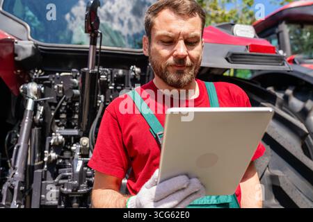 Männlicher Landwirt, der in der Nähe des Traktors im Freien in ländlichen Gebieten an einem digitalen Tablet arbeitet Stockfoto