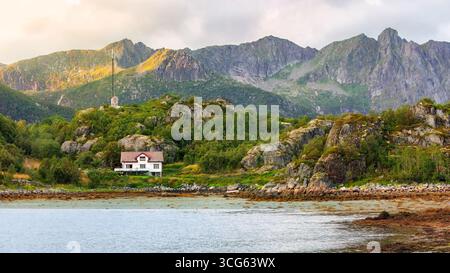Malerische Küstenlandschaft mit einem charmanten Haus eingebettet zwischen felsigen Hügeln und üppigem Grün, mit majestätischen Bergen im Hintergrund, Cap Stockfoto