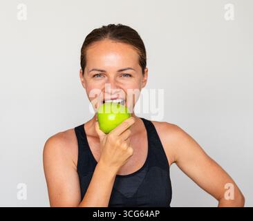 Porträt einer jungen erwachsenen Sportlerin beim Verzehr von grünem Apfel Stockfoto