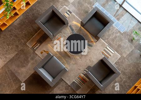 Ein Blick von oben auf einen modernen Tagungsbereich in der Hotellobby mit vier bequemen Sesseln und einem Tisch, alle auf einem weichen Teppich. Stockfoto