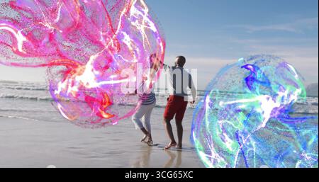 Tanzendes reifes Paar, das sich in rosa und blauen Tönen auf die wirbelnden Energiekugeln am Strand zubewegt Stockfoto