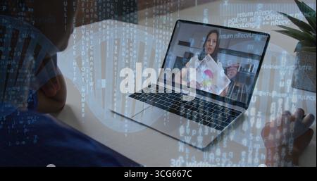 Zeigt den Laptop-Lehrer in Bluse, der zu Hause auf eine farbcodierte Grafik zeigt, mit Stift, Notizblock, Pflanze Stockfoto