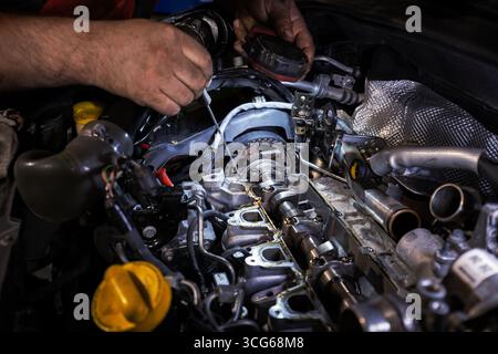 Die Hände eines Mechanikers halten eine Taschenlampe und einen Schraubendreher, während er an einem zerlegten Motor arbeitet. Die offene Motorhaube zeigt komplizierte Motorkomponenten, Stockfoto