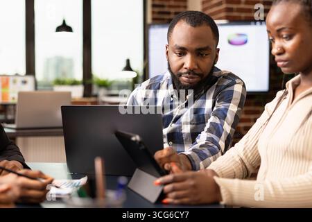 Nahaufnahme eines männlichen schwarzen Managers mit Laptop, Überprüfung der Marketingstrategie und Pläne weiblicher Mitarbeiter im Büro. afroamerikanische Geschäftsleute, die Finanzberichte erstellen und analysieren. Stockfoto