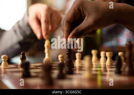 Selektiver Fokus auf das laufende Schachspiel, das die Intensität des Freundschaftsspieltags einfängt. Nahaufnahme von kaukasiern und afroamerikanern, die auf dem Tisch Figuren auf dem Schachbrett bewegen. Stockfoto