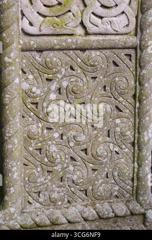 Eine Steinschnitzerei mit spiralförmigem Design. Die Schnitzerei ist mit Moos bedeckt und hat ein verwittertes Aussehen Stockfoto