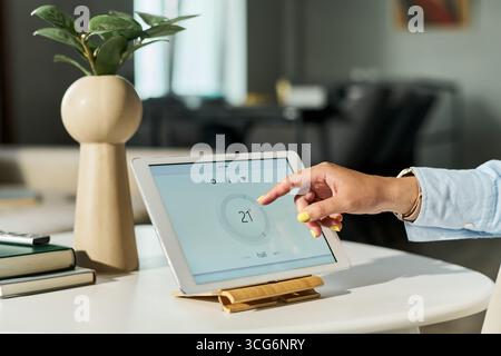 Kaukasische junge Erwachsene Frau, die ein Tablet benutzt, das das Smart Home System steuert, Hand mit digitaler Schnittstelle auf dem Bildschirm interagiert, modernes Technologiekonzept, Stockfoto
