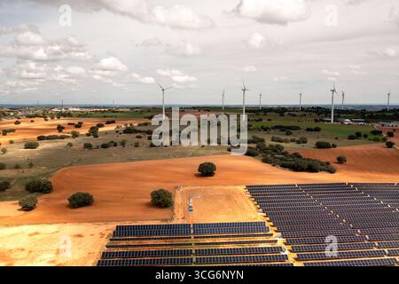 Luftaufnahmen von riesigen Solar- und Windenergieparks, die sich über grüne und rote Ackerflächen unter hellem bewölktem Himmel erstrecken, symbolisieren saubere Energie, Nachhaltigkeit und ökologische Innovation Stockfoto