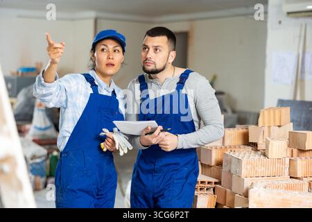 Männliche und weibliche Auftragnehmer mit Papieren, die während der Renovierung im Gebäude diskutiert werden Stockfoto