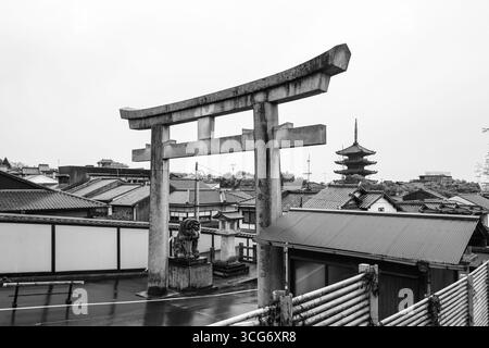 Ein Schwarzweiß-Foto des Kyoto Ryozen Gokoku-jinja Torii Tores, gesehen neben einer ruhigen Pagode. Die Szene zeigt traditionelle Architektur und Stockfoto