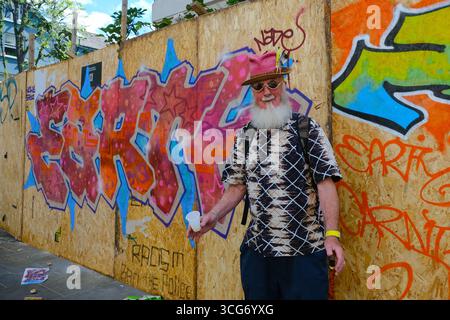 Ein Teilnehmer des Notting Hill Carnival posiert am ersten Tag des Notting Hill Carnivals vor einem Brett mit farbenfrohen Grafitti. Stockfoto