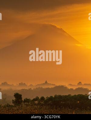 Beobachten Sie den Sonnenaufgang hinter dem Berg Merapi, mit der Silhouette des Borobudur-Tempels im Vordergrund und schaffen Sie eine atemberaubende Szene von natürlicher und kultureller Schönheit Stockfoto