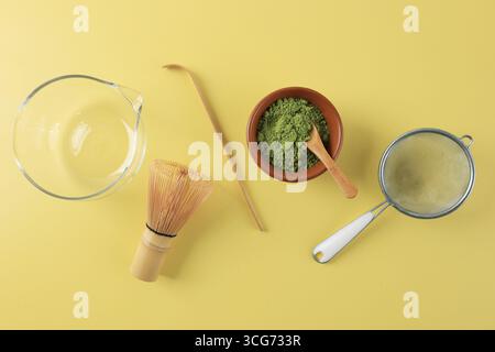 Matcha-Ausrüstung, Chasen, Löffel, Schüssel, Matcha-Pulver und Sieb. Draufsicht auf gelbem Hintergrund Stockfoto