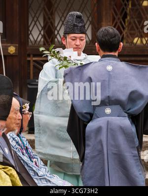 Shinto-Priester, der einen Reinigungsritus durchführt, während er einen speziellen Zweig namens Haraigushi mit shide, einem zickzackförmigen Papierstreamer, hält Stockfoto