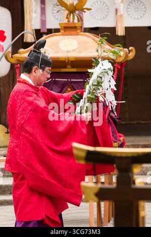 Shinto-Priester, der einen Reinigungsritus durchführt, während er einen speziellen Zweig namens Haraigushi mit shide, einem zickzackförmigen Papierstreamer, hält Stockfoto