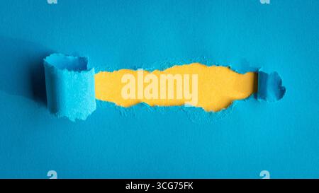 Loch in blauem Papier auf gelbem Hintergrund gerissen. Kopierbereich. Stockfoto
