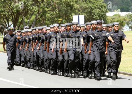 Marineschiffe in schwarzen Uniformen marschieren tagsüber in Formation durch einen Park. Stockfoto