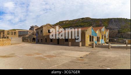 Alte Blei-, Silber- und Zinkbergbauanlage in Argentiera, Sardinien, mit verwitterten Gebäuden und farbenfrohen Wandmalereien inmitten einer zerklüfteten Hügellandschaft. Stockfoto