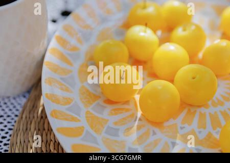 Gelbe Pflaumen und Tasse auf Sommer-Picknicktisch mit Tageslicht Stockfoto