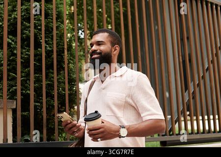 Ein gut gekleideter Afroamerikaner erkundet eine moderne Stadt bei einem Kaffee. Stockfoto