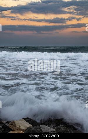 Ozeanwellen, die bei Sonnenuntergang gegen Felsen krachen Stockfoto