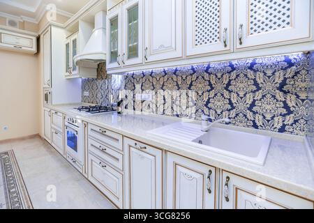 Eine Küche mit weißen Schränken und einer blau-goldenen Wand. Die Theke ist weiß und das Waschbecken weiß Stockfoto
