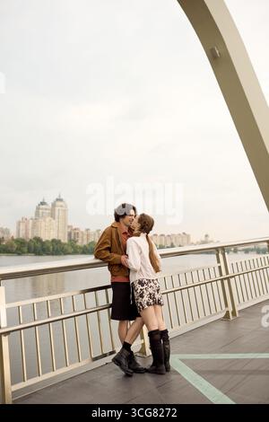 Ein junges Paar umarmt sich glücklich, während es einen Spaziergang auf einer malerischen Brücke in der Nähe des Wassers macht. Stockfoto