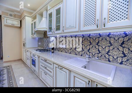 Eine Küche mit weißen Schränken und einer blau-goldenen Wand. Die Theke ist weiß und das Waschbecken weiß Stockfoto