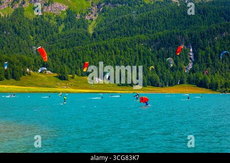 Kitesurfen und Wingsurfen auf dem Alpensee Silvaplana an einem sonnigen Sommertag mit Berg in Silvaplana, Maloja, Graubünden, Schweiz. Stockfoto