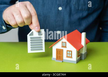 Ein Mann hält eine Urkunde in der Nähe seines Hauses. Mietvertrag für Wohnimmobilien. Eigentumsrechte, Hypothekenvertrag, Eigentum, legale Wohnungsdokumente Stockfoto