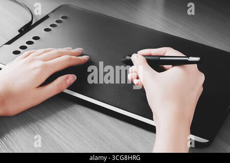 Weibliche Hände zeichnen auf einem Grafiktablett. Designer Hand hält einen Stift und zeichnet auf einem Tablet Stockfoto