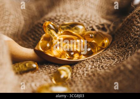 Fischöl-Kapseln auf einem Holzlöffel. Fischöl-Pillen, Tabletten auf dem Sackleinen. Vitaminkomplex Omega 3,6,9. Nahaufnahme Stockfoto