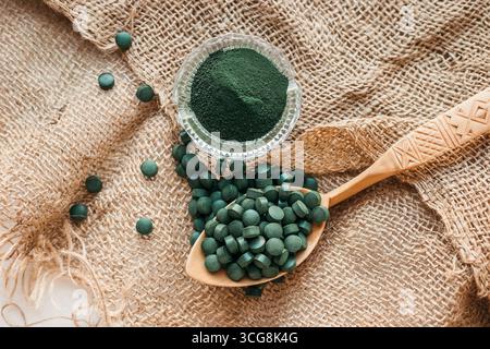 Grüne Algen-Spirulina in Tabletten und Pulver auf einem Sackleinen-Hintergrund. Draufsicht Stockfoto