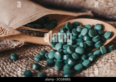 Löffel in Tabletten von Spirulina-Algen in Tabletten auf dunklem Sackleinen Hintergrund. Veganes Superessen Stockfoto