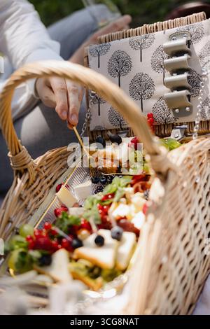 Ein wunderschön gestalteter Korb mit lebendigen Früchten, Gourmet-Snacks und frischem Gemüse lädt zu einem Moment der Freude in der Sonne ein. Stockfoto