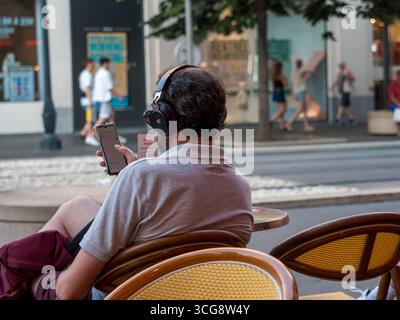 Nizza, Frankreich, 8. August 2025. Mann mit Smartphone und Kopfhörern, der im Straßencafé sitzt Stockfoto